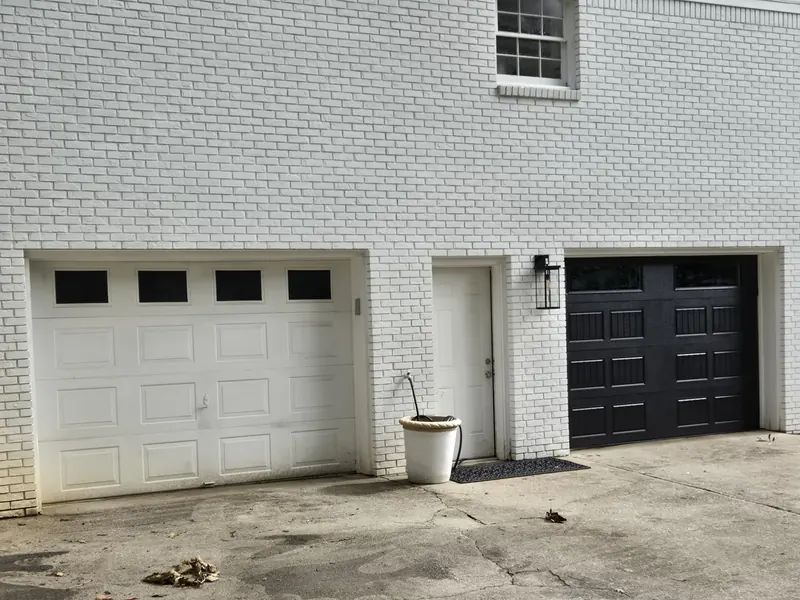 A white brick house with one white garage door and one black one